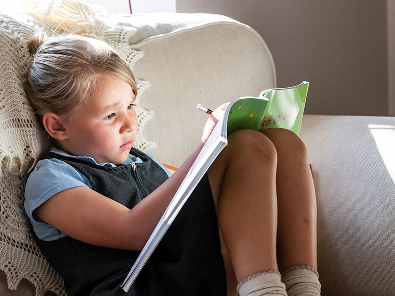 Image of young girl sat on sofa writing in book